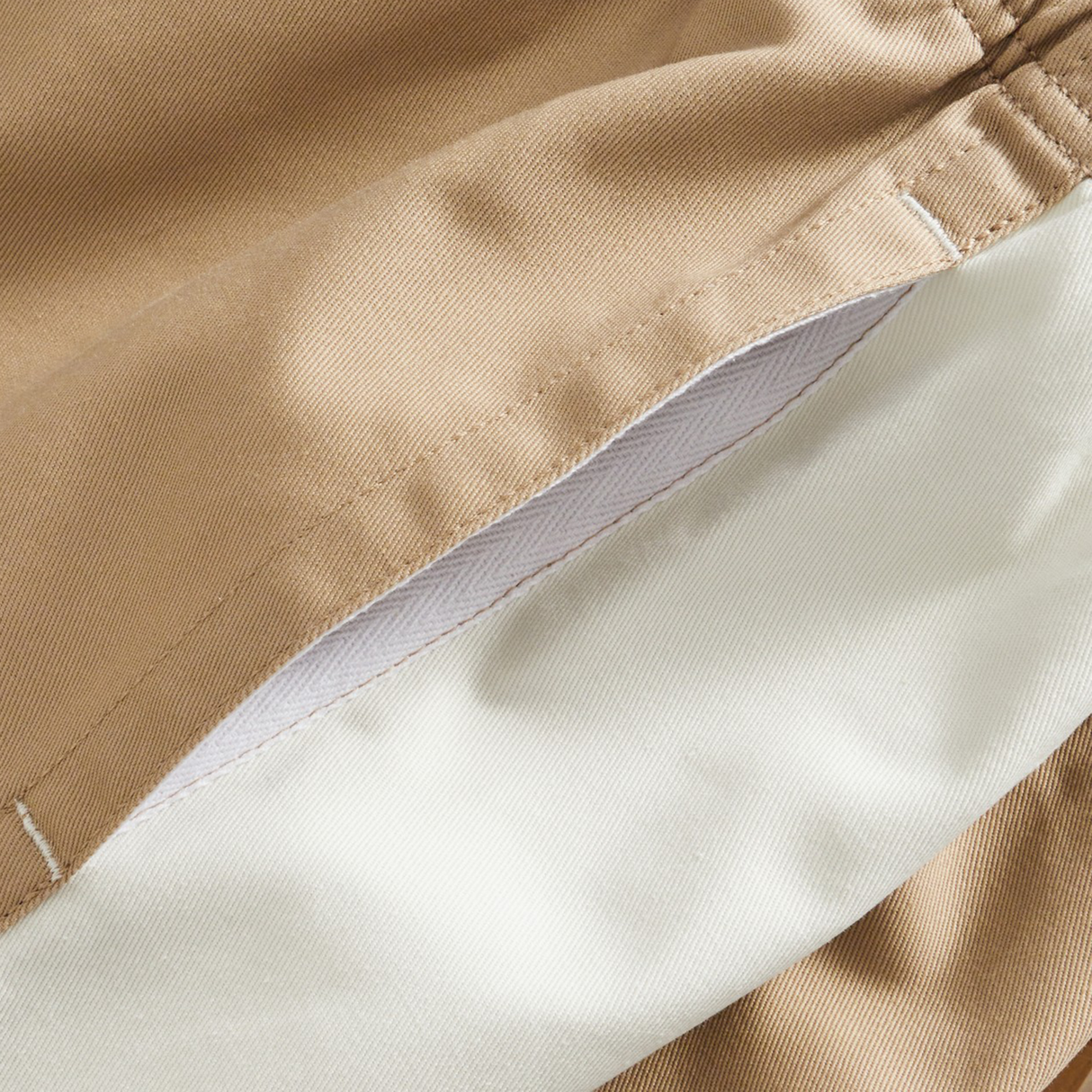 Close-up of beige fabric with white lining and visible stitching, likely the inside pocket of the Fundamental Harlequin Drill 3" Shorts by Canterbury.