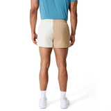A person stands facing away against a white background, wearing a blue shirt, white shoes and socks, and Canterbury Fundamental Harlequin Drill 3" Shorts in two-tone beige and white.