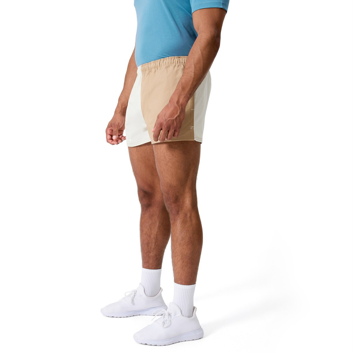 A person wearing a blue t-shirt, Canterbury's Fundamental Harlequin Drill 3" Shorts, white socks, and white sneakers stands against a plain white background.