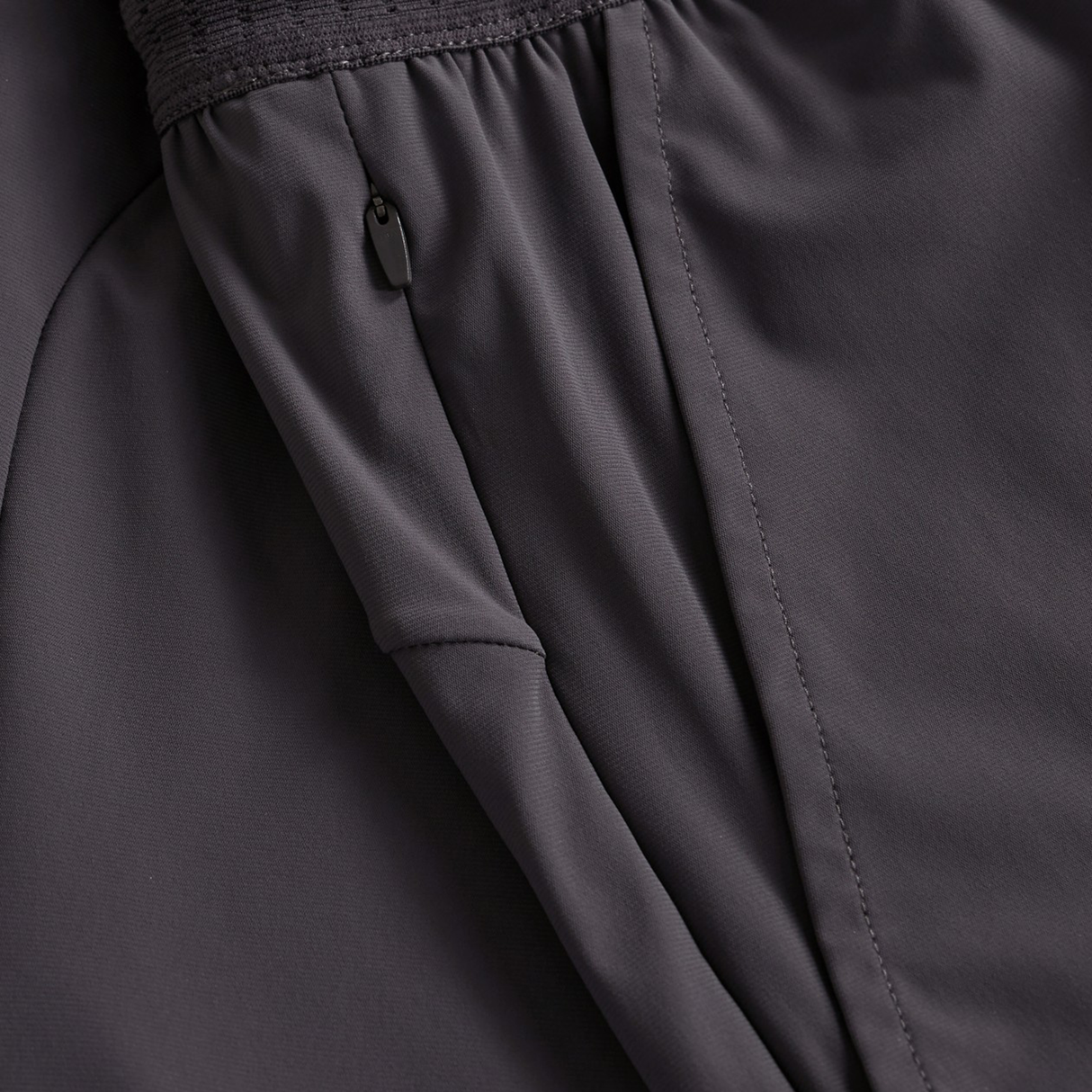 Close-up of Everest Woven Shorts by Canterbury, featuring a dark gray color, zippered pocket, and elastic waistband.