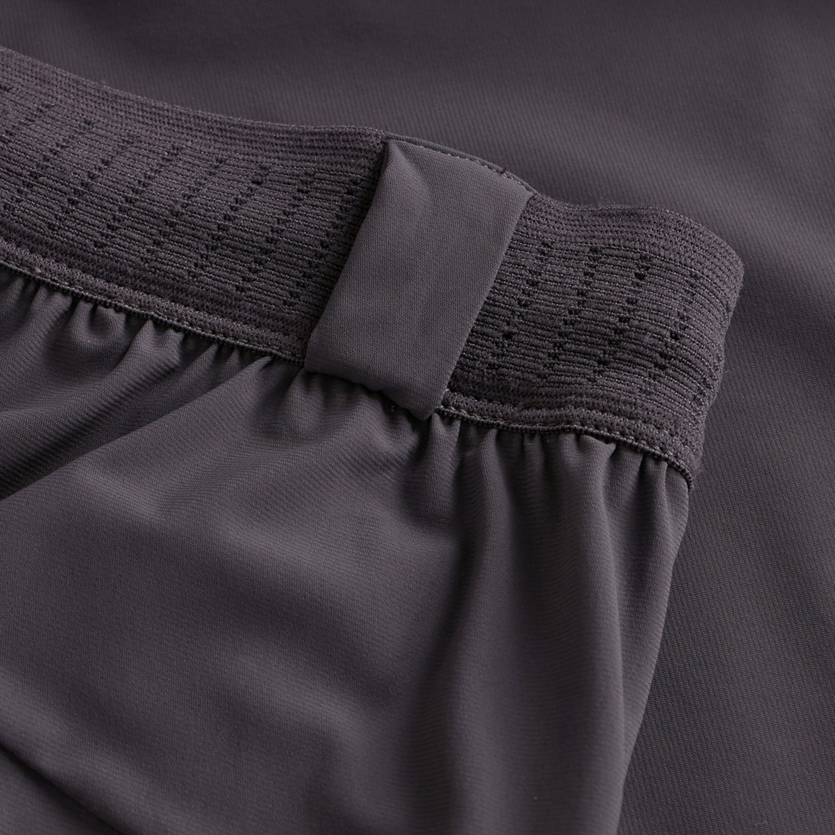 Close-up of a dark grey elastic waistband with a fabric loop detail, highlighting texture and stitching on the Canterbury Everest Woven Shorts, plus the smooth fabric beneath.