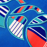 Close-up of blue fabric from Canterbury's Uglies Tactic Short, highlighting an embroidered abstract design with curved red, white, blue, and teal stripes, all outlined in teal stitching.