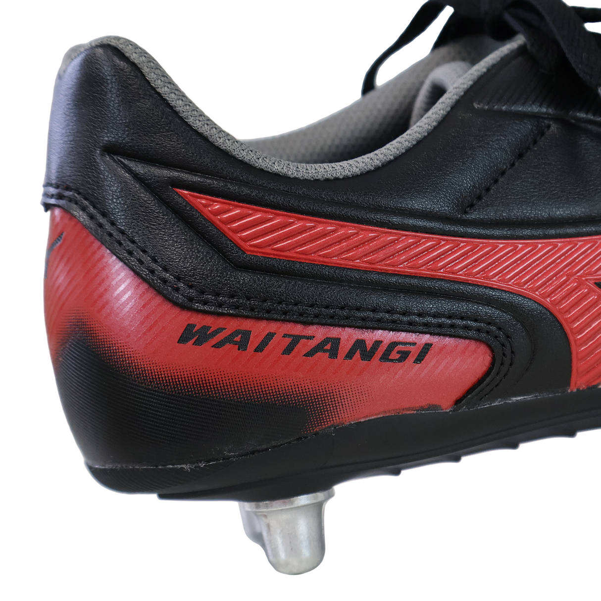 A close-up of the Mizuno Waitangi II CL SG Black/Morelia 40th Anniversary Red rugby boot with "WAITANGI" on the side and a metal stud on the sole—perfect for players needing soft ground rugby boots.