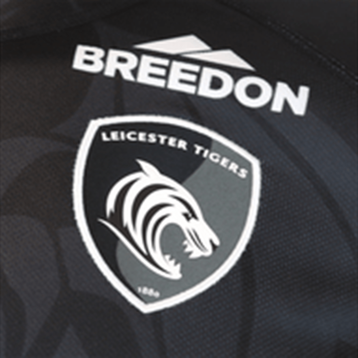 Close-up of a breathable Samurai Leicester Tigers Change Jersey 23/24 featuring the team logo and the sponsor, Breedon, on a textured black fabric.