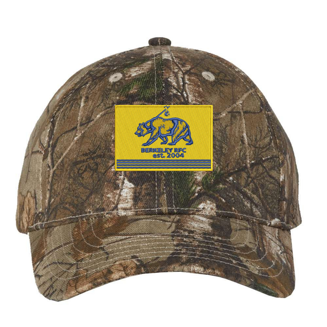 Berkeley RFC Realtree Camo Cap featuring a yellow rectangular patch with a blue bear, the text “BERKELEY RFC est. 2004”, and blue horizontal stripes.