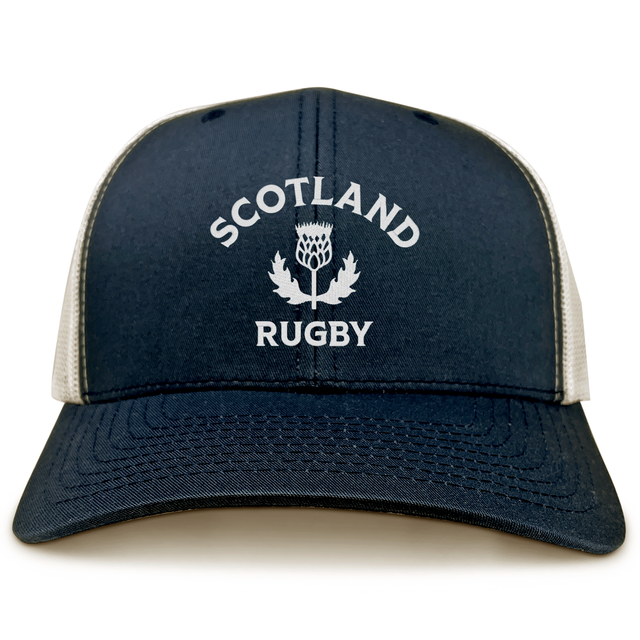 The EMB S&S Activewear Nations of Rugby Scotland Retro Trucker Cap features navy and white colors with "Scotland Rugby" and a thistle emblem printed on the front.