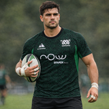 A male rugby player holding a ball stands on a grassy field, wearing the Las Serpientes Mexico Rugby Training Jersey by Credo Rugby—a green and black jersey with white logos.