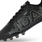 The Ida Women's Rise Club FG "Stronger Together" cleat by IDA Sports offers adjustable laces and is made from vegan leather. This black shoe with white accents and large "IDA" text on the side is designed for style and comfort, perfect for women's soccer enthusiasts.