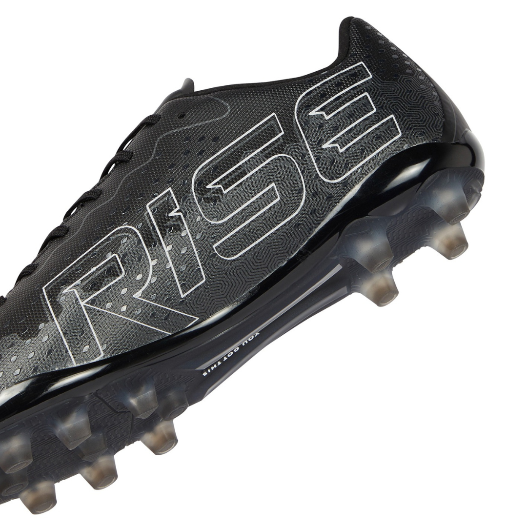 Close-up of the Ida Women's Rise Club FG "Stronger Together" cleat by IDA Sports, in black vegan leather with "RISE" on the side and transparent studs for traction.
