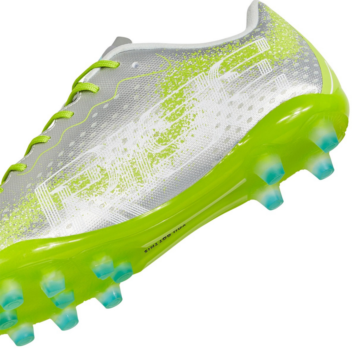 The Ida Women's Rise Club FG "Play All Day" by IDA Sports is a silver and neon green firm ground cleat with vegan leather, featuring blue-tipped studs and yellow laces.