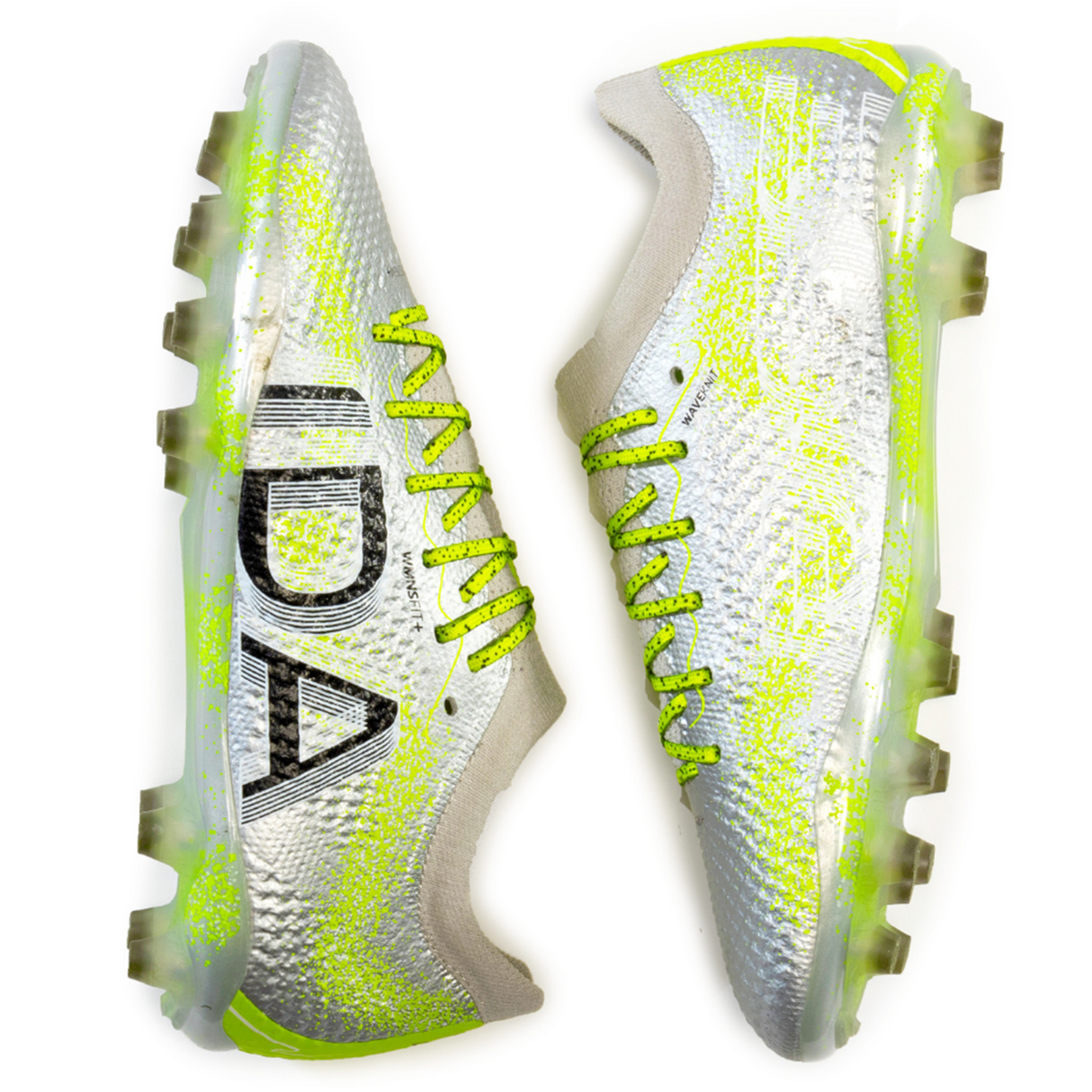 A pair of Ida Women's Rise Elite FG "Play All Day" soccer cleats by IDA Sports in silver and green featuring textured surfaces for enhanced ball control, with black lettering on the side and neon yellow laces.