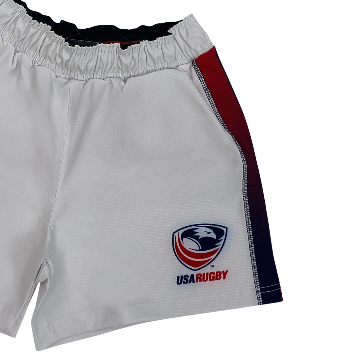 The USA Rugby Pro Home Short by Castore features an elastic waistband, the USA Rugby logo on the lower right, and bold red and blue side stripes. Made from moisture-wicking fabric, these Castore shorts offer comfort and style both on and off the field.
