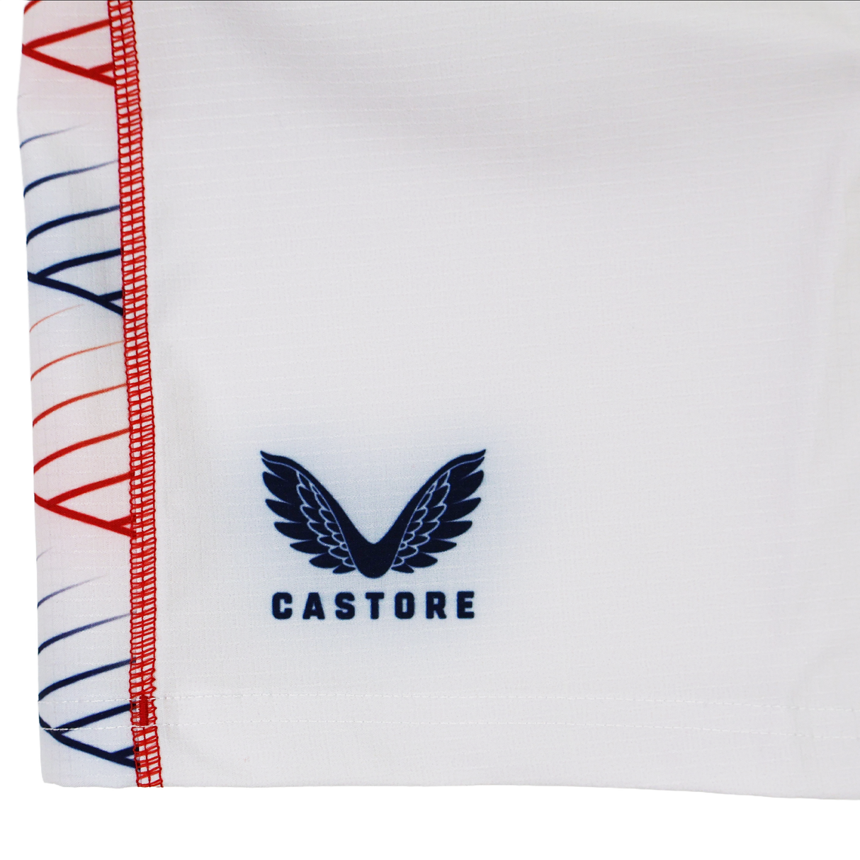 Close-up of the Women's USA Rugby 22/23 RWC Home Pro Short by Castore, showing white fabric with the Castore logo in navy blue and decorative red and blue stitching along the edge.
