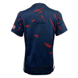 Back view of the Women's USA Rugby Authentic Home Jersey by Castore in navy blue with abstract red and dark blue patterns. The left sleeve features an American flag patch. Crafted from moisture-wicking fabric, it ensures athletes stay dry and comfortable during intense gameplay.