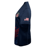 Side view of a navy blue Women's USA Rugby 2024 Olympic 7's Jersey by Castore, featuring a USA shield emblem on the chest and an American flag on the sleeve. Made from performance fabric, it has striking red and white stripes on the front.