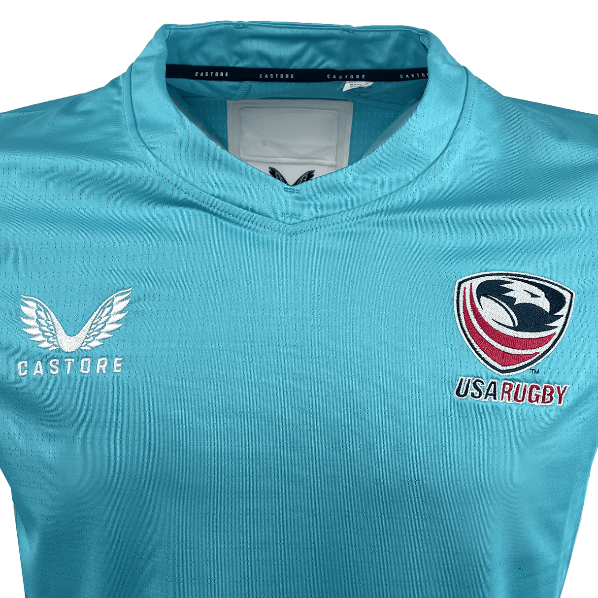 This Women's USA Rugby Pro Training Jersey by Castore is light blue, featuring both the USA Rugby and Castore logos on the chest, and is crafted with moisture-wicking fabric for ultimate comfort.