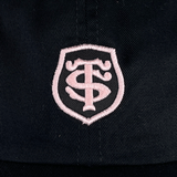 A black and pink adjustable hat features a white embroidered shield-like emblem with stylized letters "TS" intertwined, reminiscent of the Stade Toulousain Heritage 86 Cap by Nike design.