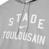 The Nike Stade Toulousain 25/26 Premium Pullover Hoodie features a gray design with white drawstrings, "STADE TOULOUSAIN" text, and a white Nike swoosh on the front—ideal for rugby fans.