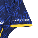 Close-up of the Leinster 25/26 Third Pro Shirt by Castore: dark blue sleeve with wavy light blue patterns, yellow trim, and white "Bank of Ireland" logo—engineered by Castore for top rugby performance.