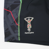 Close-up of the Harlequins 22/23 3rd Pro Short by Castore, highlighting bold red, green, and black geometric patterns along with the Castore logo and text.