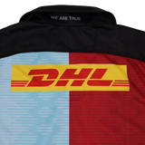 The Castore Harlequins Replica Home Jersey 22/23 features "WE ARE TRUE" on the collar, blue and red Harlequin-inspired panels, and a bold yellow and red DHL logo across the back.