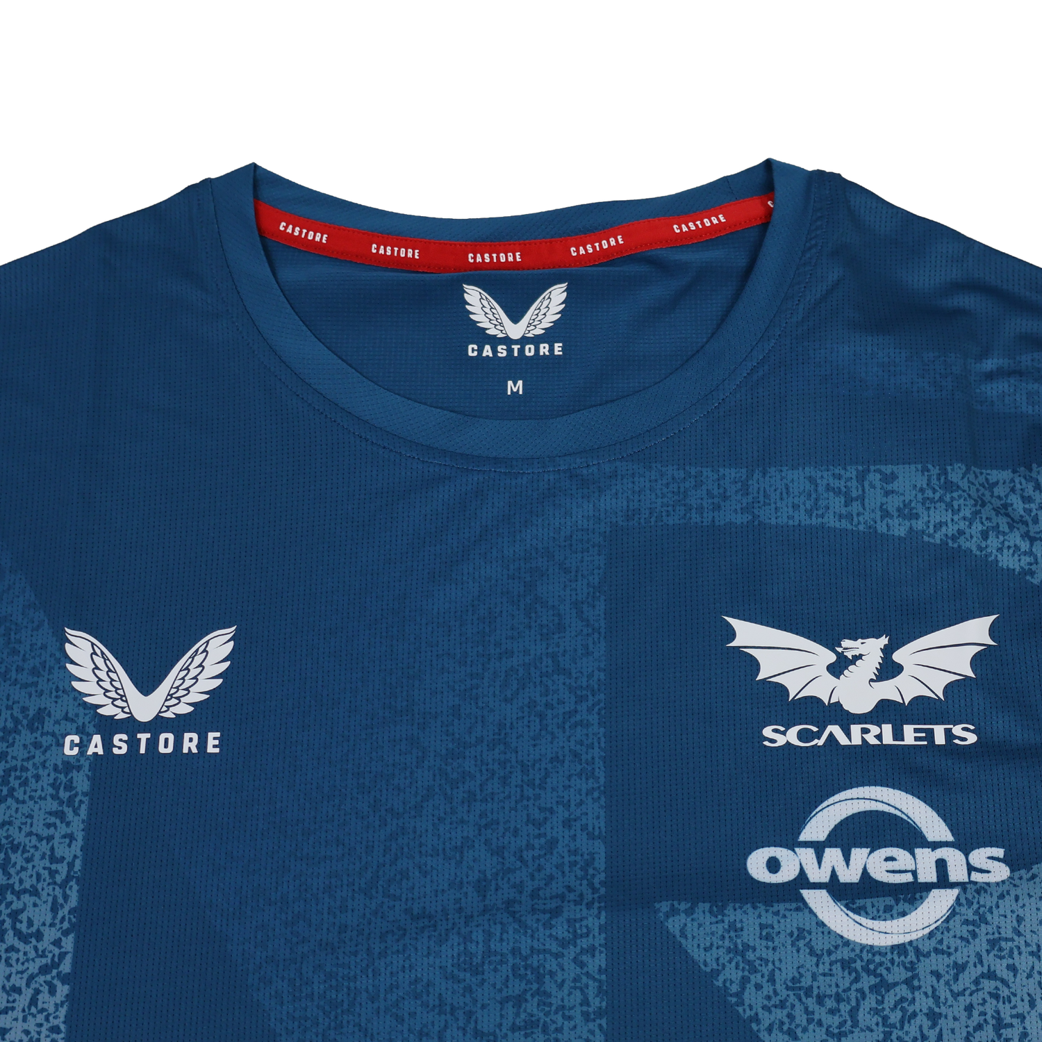 Close-up of the Scarlets Training Tee 22/23 by Castore, a blue performance shirt featuring the Castore logo, Scarlets rugby emblem, and Owens sponsor on the chest.