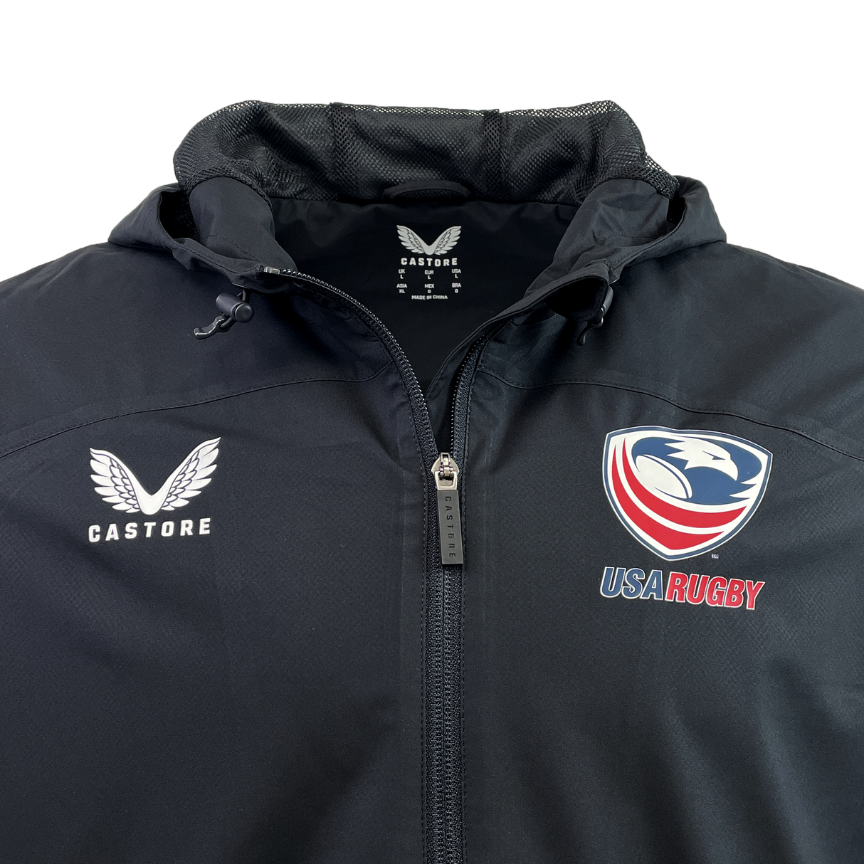 The USA Rugby Rain Jacket by Castore is a black zip-up featuring the USA Rugby emblem on the right and the Castore logo on the left, with lightweight mesh lining and water-resistant technology for comfort and protection.