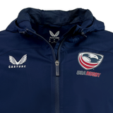 Close-up of the USA Rugby Rain Jacket by Castore in navy blue, showcasing the Castore logo on the left and USA Rugby emblem on the right. This water-resistant jacket includes a zipper, hood, and lightweight mesh lining for comfort and durability.