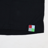 A close-up of the hem of a black Castore Harlequins 22/23 Heritage Cotton Tee, showing a small square tag with red, light blue, gray, and green quadrants.