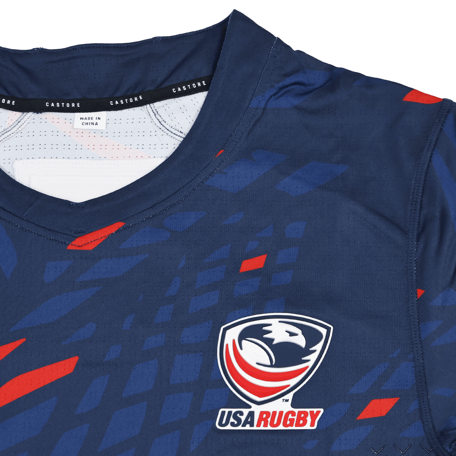 The Castore USA Rugby 23/24 Pro Home Jersey is a navy rugby shirt with red and blue geometric patterns, featuring the USA Rugby logo and a Castore collar label—a must-have for men's rugby fans.