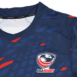 The Castore USA Rugby 23/24 Pro Home Jersey is a navy rugby shirt with red and blue geometric patterns, featuring the USA Rugby logo and a Castore collar label—a must-have for men's rugby fans.