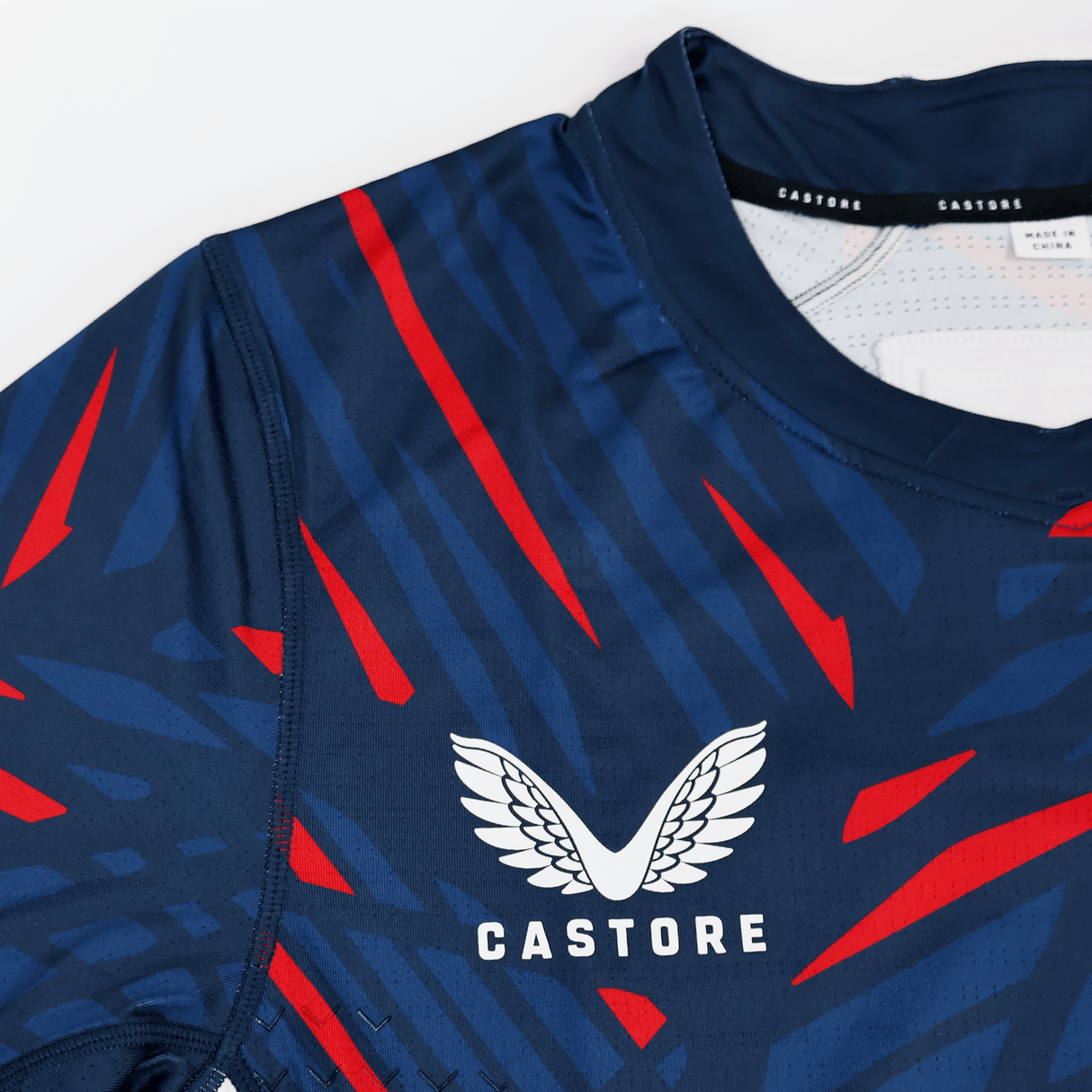Close-up of the USA Rugby 23/24 Pro Home Jersey by Castore, a navy blue men's rugby shirt with red and light blue stripes, featuring the Castore logo and brand name on the chest.