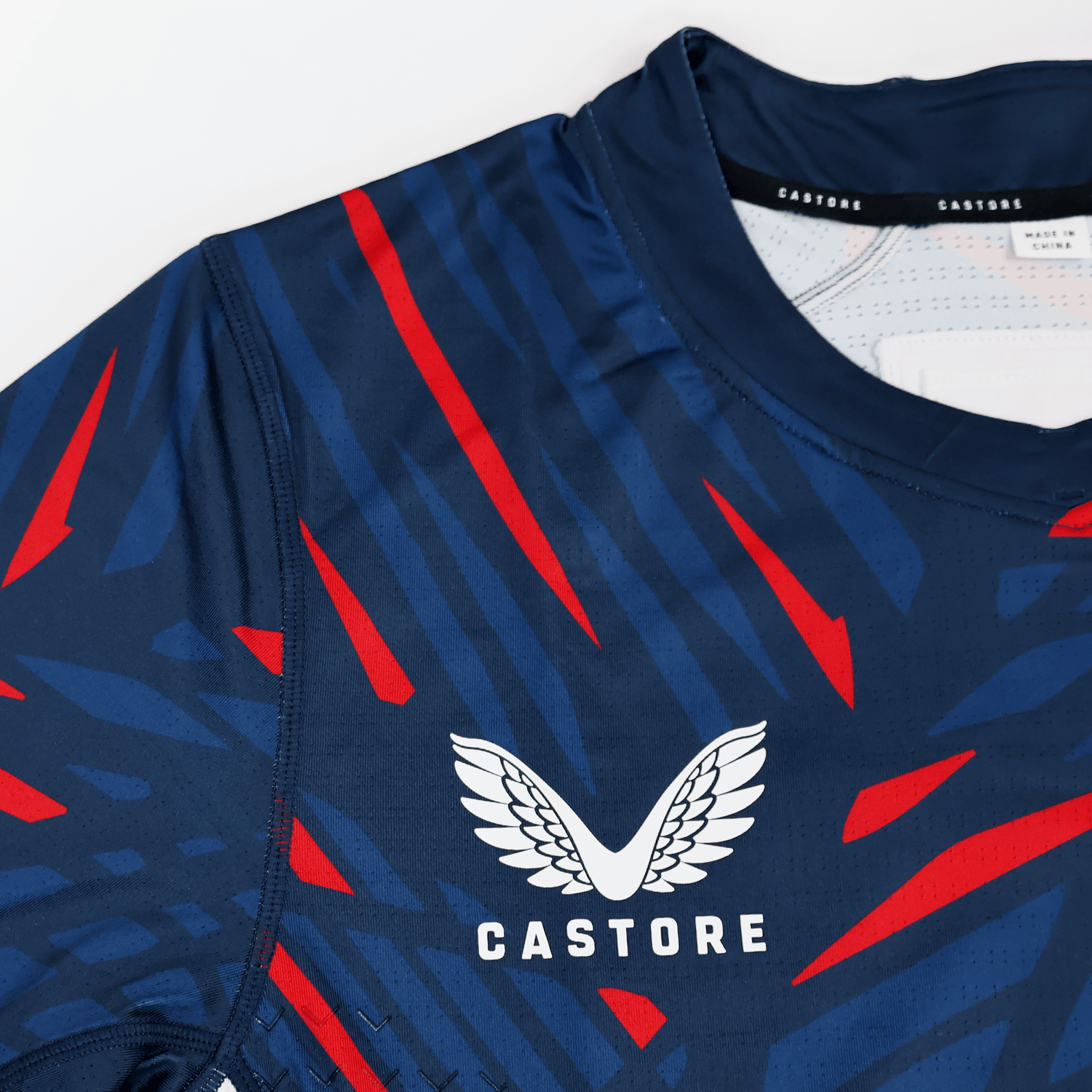 Close-up of the USA Rugby 23/24 Pro Home Jersey by Castore, a navy blue men's rugby shirt with red and light blue stripes, featuring the Castore logo and brand name on the chest.