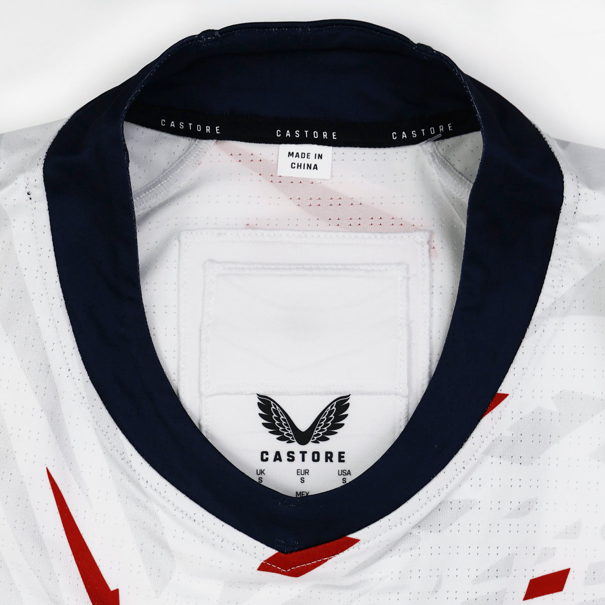 Close-up of the USA Rugby 23/24 Pro Away Jersey by Castore in white with a dark collar, showing the Castore brand label, care instructions, and "Made in China" tag inside the neckline—official team apparel.