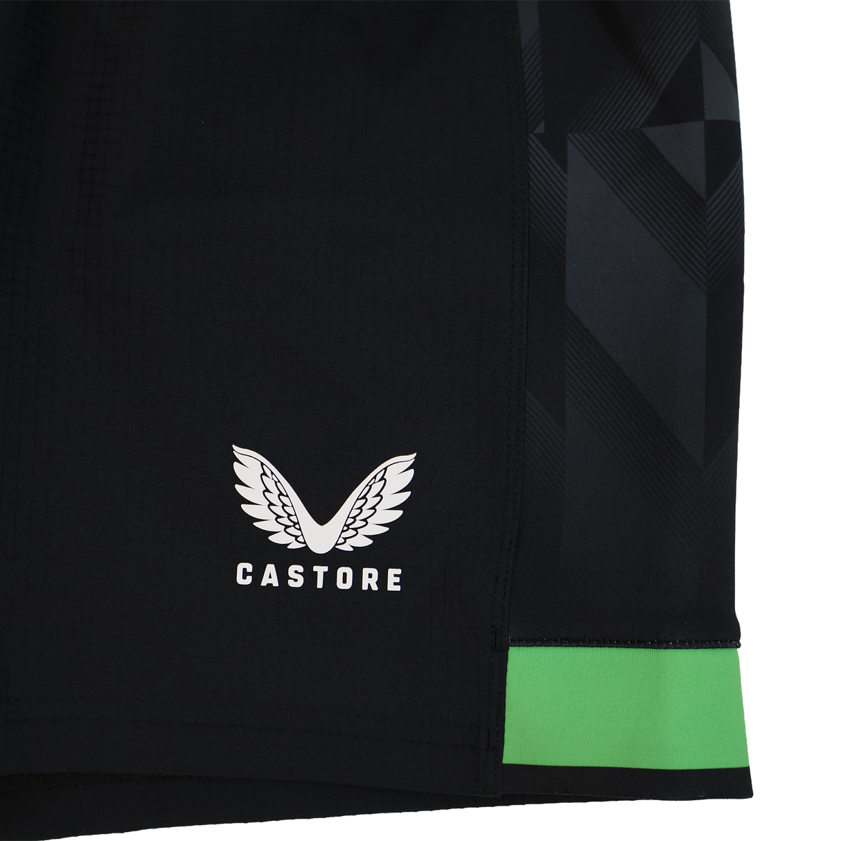 Close-up of the Harlequins 23/24 Home Shorts by Castore: black rugby shorts with a white winged Castore logo, a green band near the hem, and a geometric side pattern—part of Castore’s official collection.