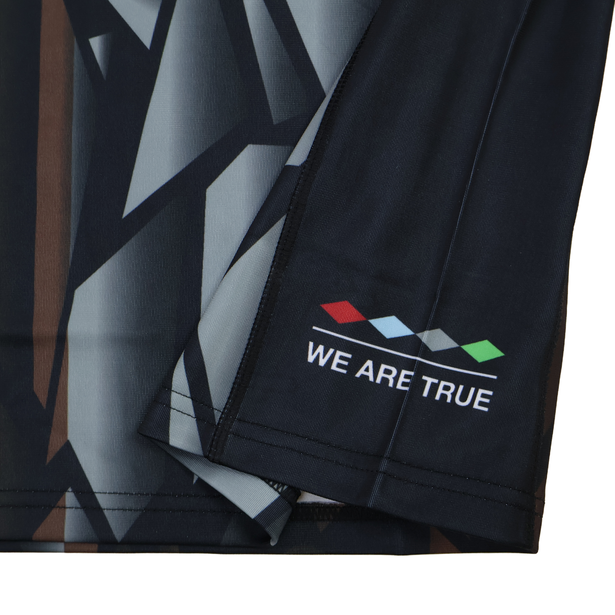 Close-up of the Harlequins 23/24 Replica Third Jersey by Castore, showing a dark geometric fabric with four colored diamonds and "WE ARE TRUE" near the hem—designed as a moisture-wicking football jersey.