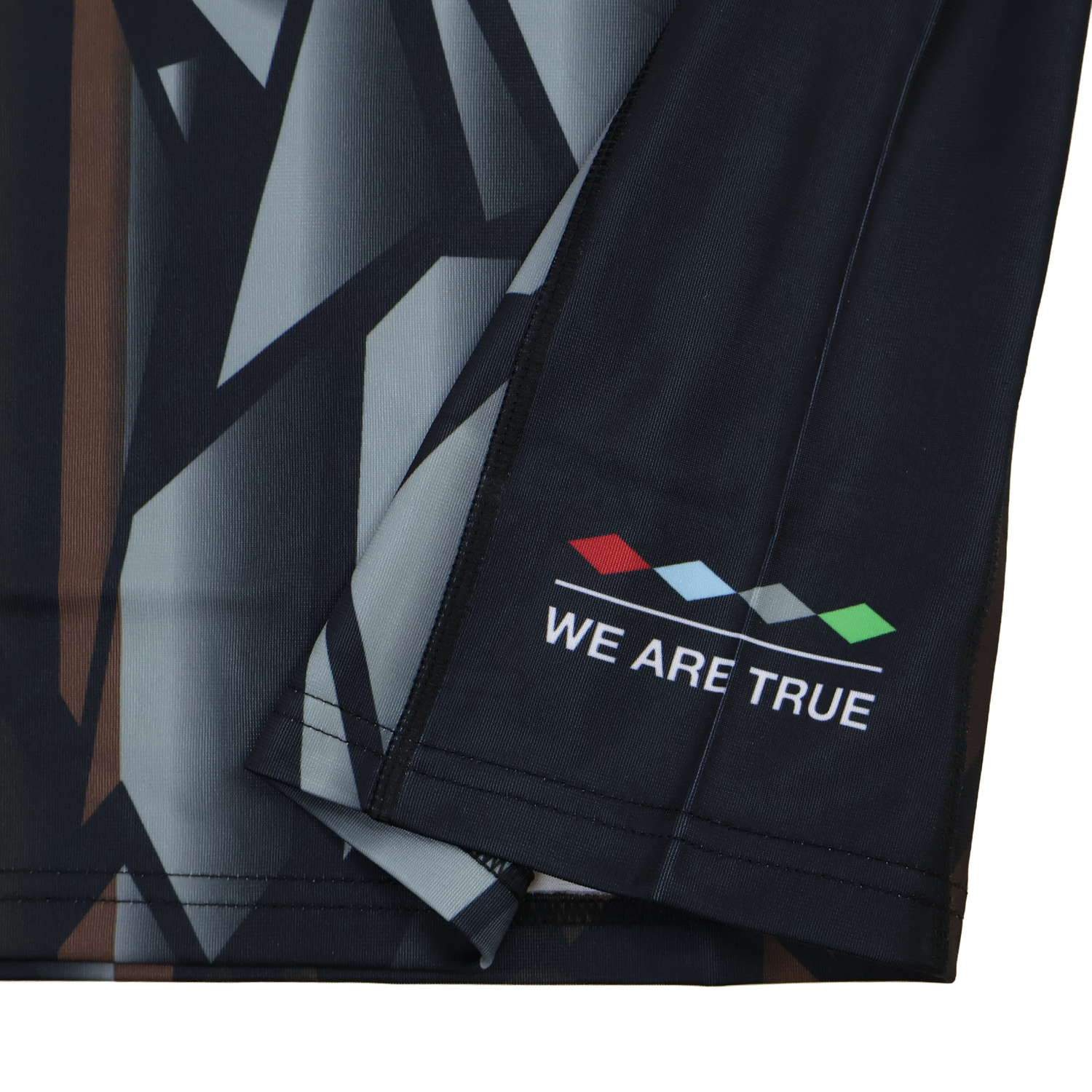 Close-up of the Harlequins 23/24 Replica Third Jersey by Castore, showing a dark geometric fabric with four colored diamonds and "WE ARE TRUE" near the hem—designed as a moisture-wicking football jersey.