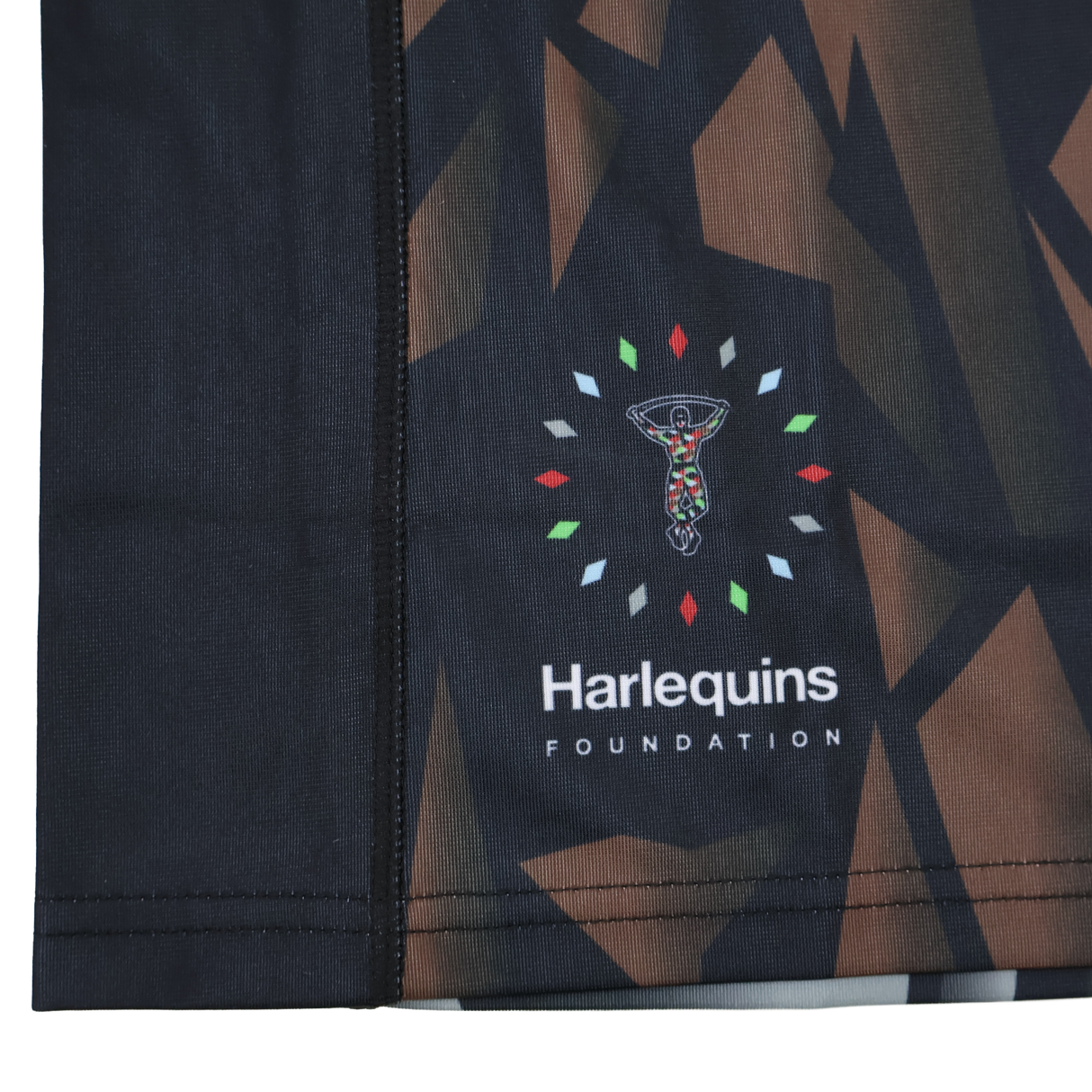Close-up of the moisture-wicking fabric on the Castore Harlequins 23/24 Replica Third Jersey, showing its abstract geometric pattern and Harlequins Foundation logo with stylized figure amid colored shapes.
