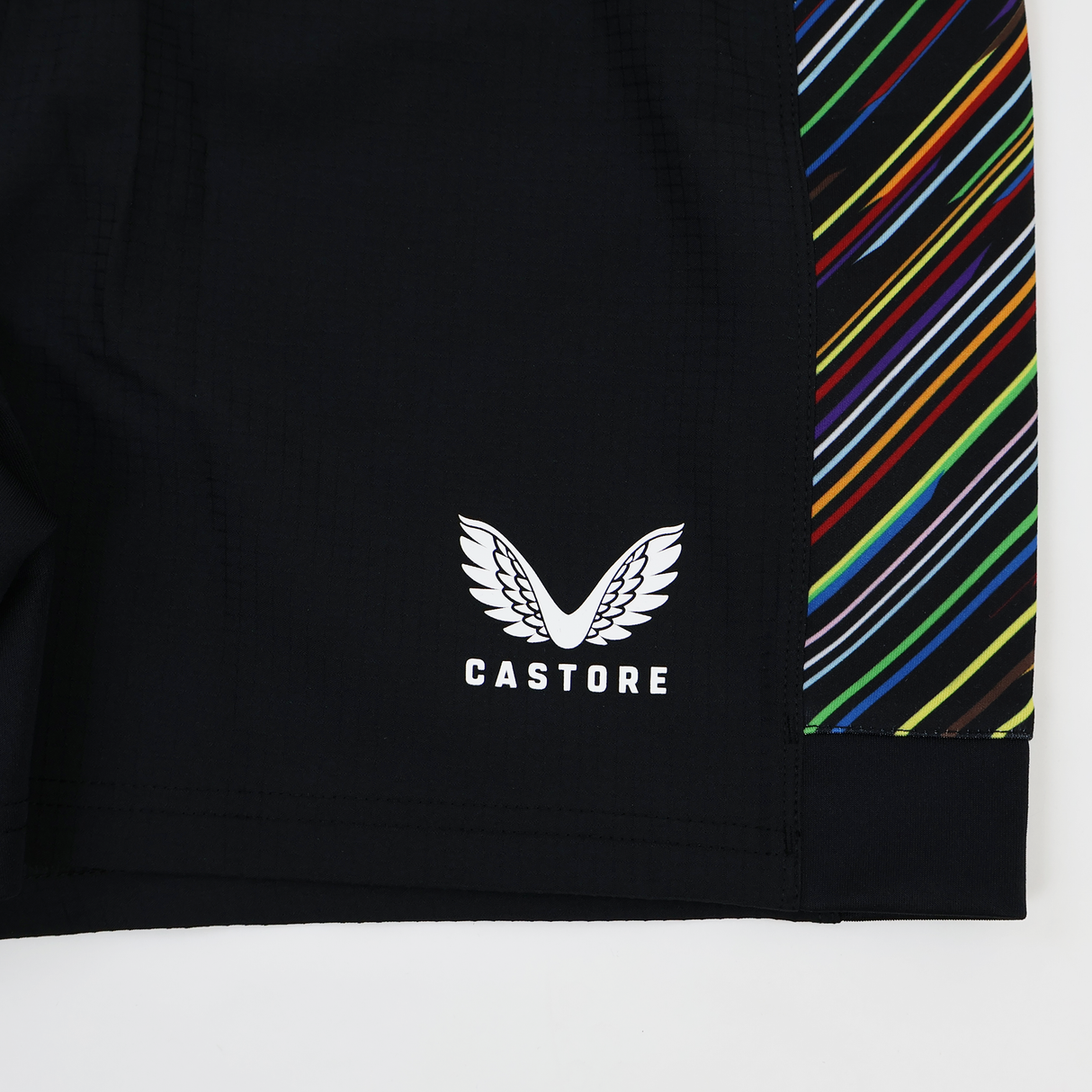 Close-up of the Harlequins 23/24 Pro Pride Short by Castore, showing the white Castore logo and name on black fabric, plus a vibrant side panel with colorful diagonal stripes.