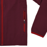 A close-up of the Scarlets 23/24 Travel Jacket Men's by Castore displays its maroon fabric and red side pocket zipper, highlighting part of the front and one sleeve against a white background.
