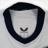 The USA Rugby 24/25 Pro Away Jersey by Castore features white fabric with a navy collar, showcasing the Castore logo, size chart, and a "Made in China" label inside the neck.
