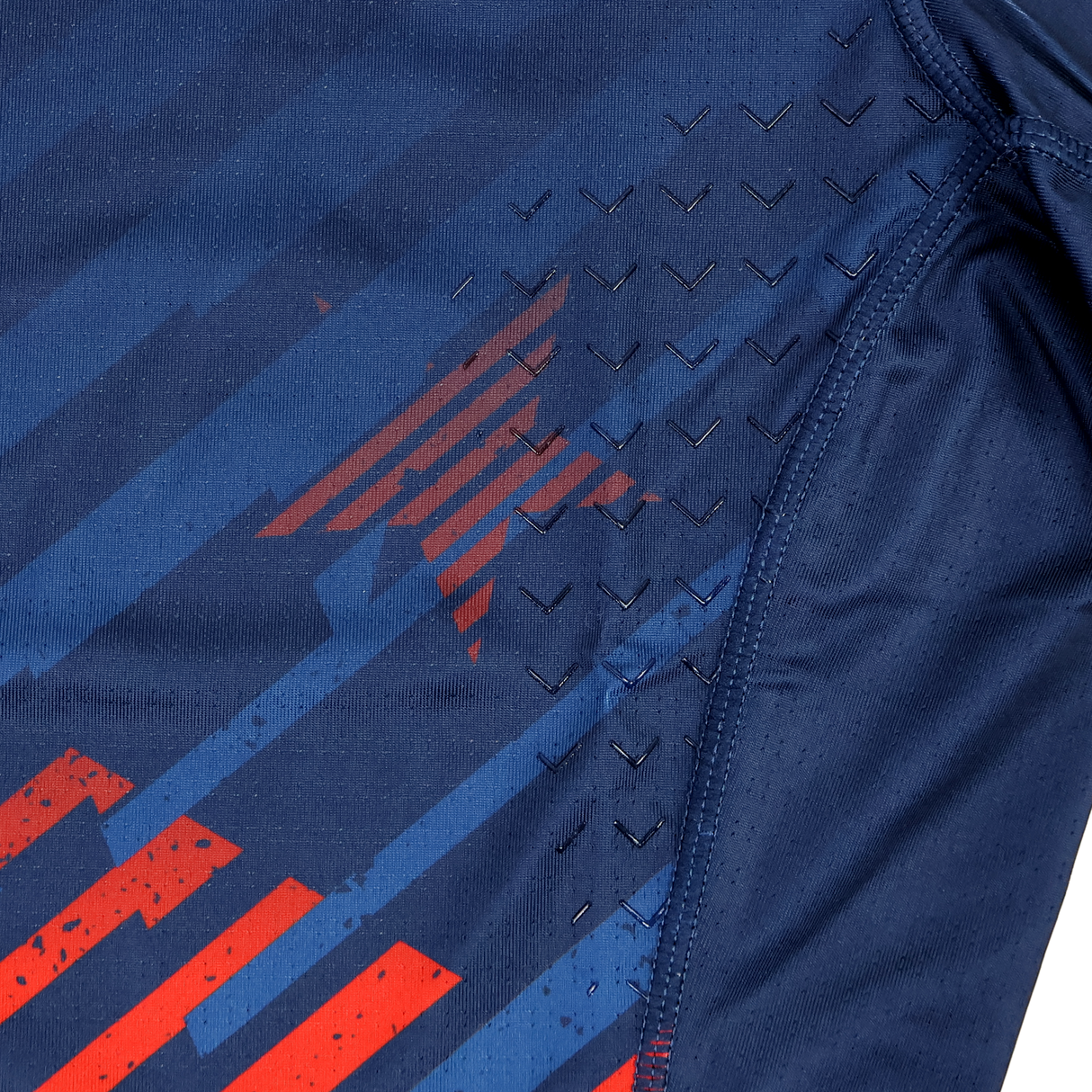 Close-up of the Castore USA Rugby 24/25 7s Olympic Pro Home Jersey’s navy athletic fabric, featuring red stripes, a subtle star pattern, and black chevron-textured grips near the seam.