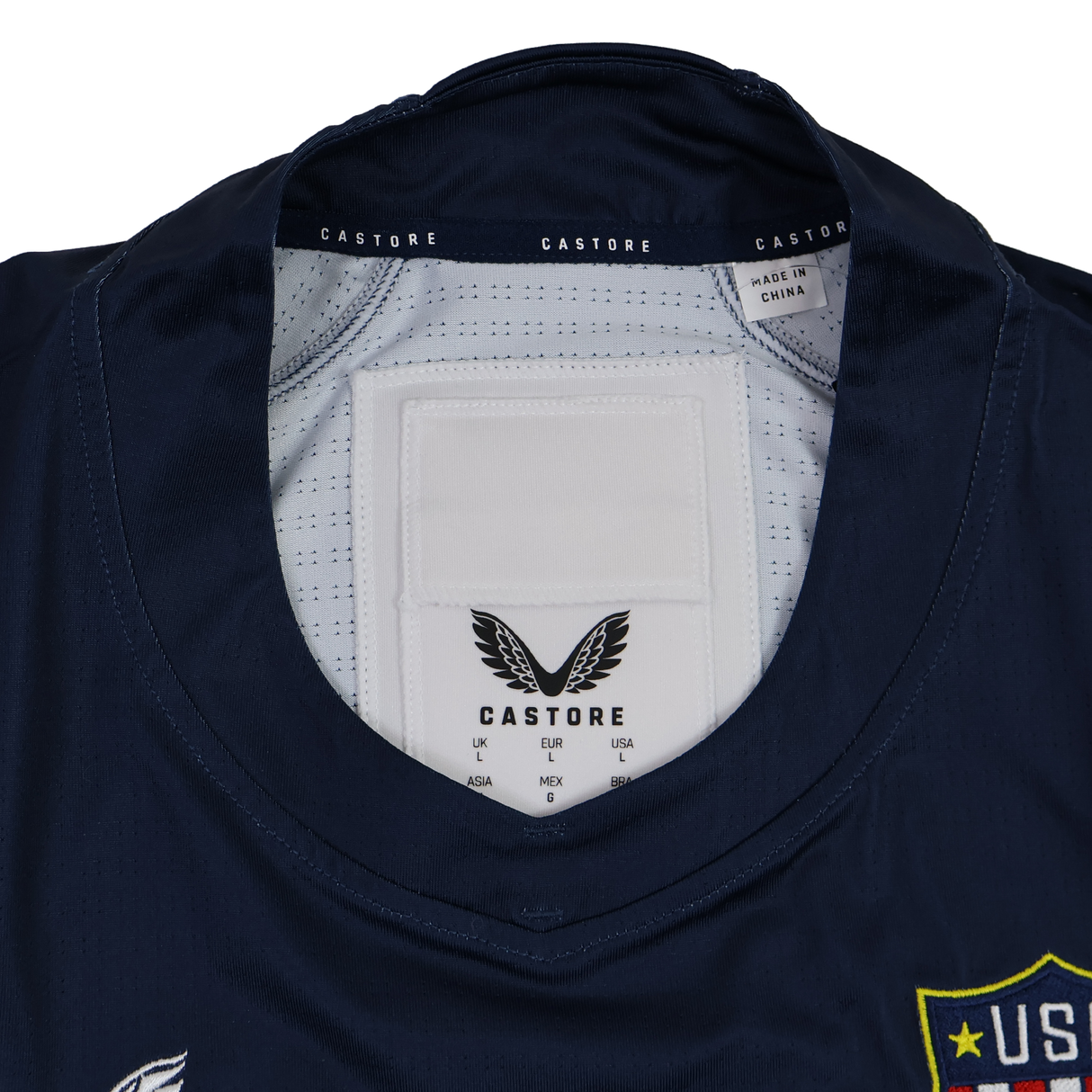 Close-up of the USA Rugby 24/25 7s Olympic Pro Home Jersey collar by Castore, showing the brand label, size tags, and "Made in China" text. A portion of the USA Rugby badge is visible on the right.