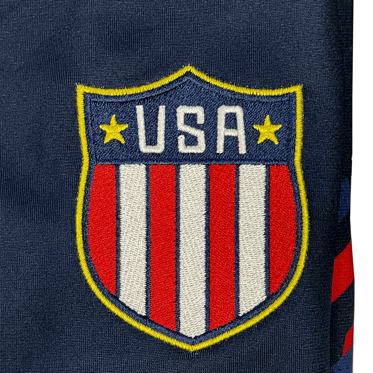 Embroidered USA shield patch with two yellow stars and red, white, and blue stripes on navy—ideal for Eagles fans or pairing with the USA Rugby 24/25 Olympic 7's Jersey by Castore.
