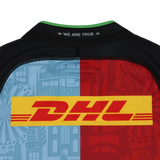 Back of the Harlequins 24/25 Pro Home Jersey by Castore, featuring a DHL logo, split light blue and red halves with cityscape designs, and "WE ARE TRUE" below the collar—a striking Castore rugby shirt.