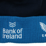 Close-up of the Leinster Bobble Beanie 24/25 by Castore, showing blue and black knit fabric with "Bank of Ireland" and logo embroidered in white—ideal detail for this official Castore beanie.