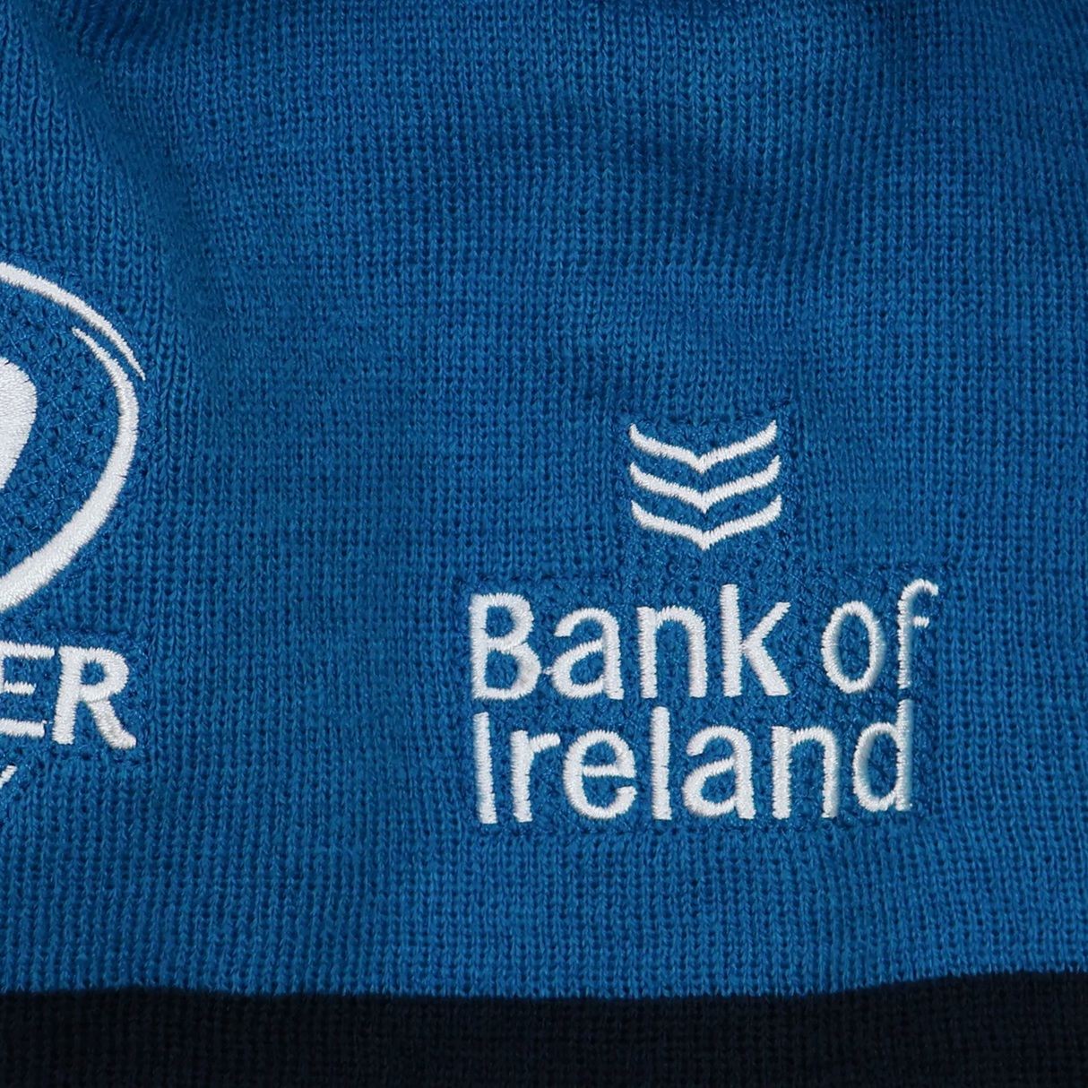 Close-up of blue fabric on the Leinster 24/25 Beanie by Castore, showing the embroidered "Bank of Ireland" logo and part of another logo in white thread.