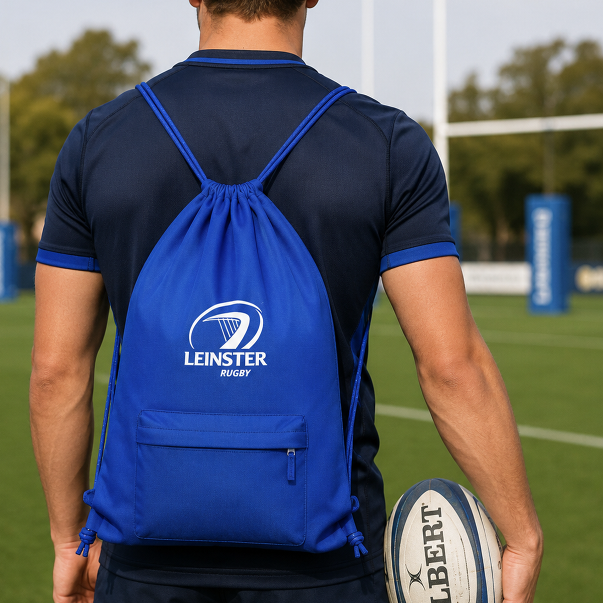 A person with the Leinster Drawstring Bag 24/25 by Castore stands on a rugby field holding a rugby ball.