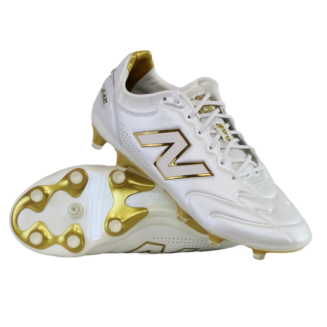 A pair of New Balance 442 Elite FG v3 soccer cleats in Sea Salt/Gold Metallic, one upright and one on its side, showcase DynamicTouch Tech for superior control and gold-accented firm ground studs.