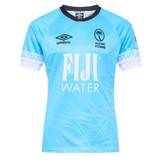 The Fiji 25/26 Replica Away Jersey by Umbro is a light blue rugby jersey with white accents, subtle Fijian masi art, "FIJI WATER" sponsor logo, Umbro branding, and the Flying Fijians emblem on the chest.